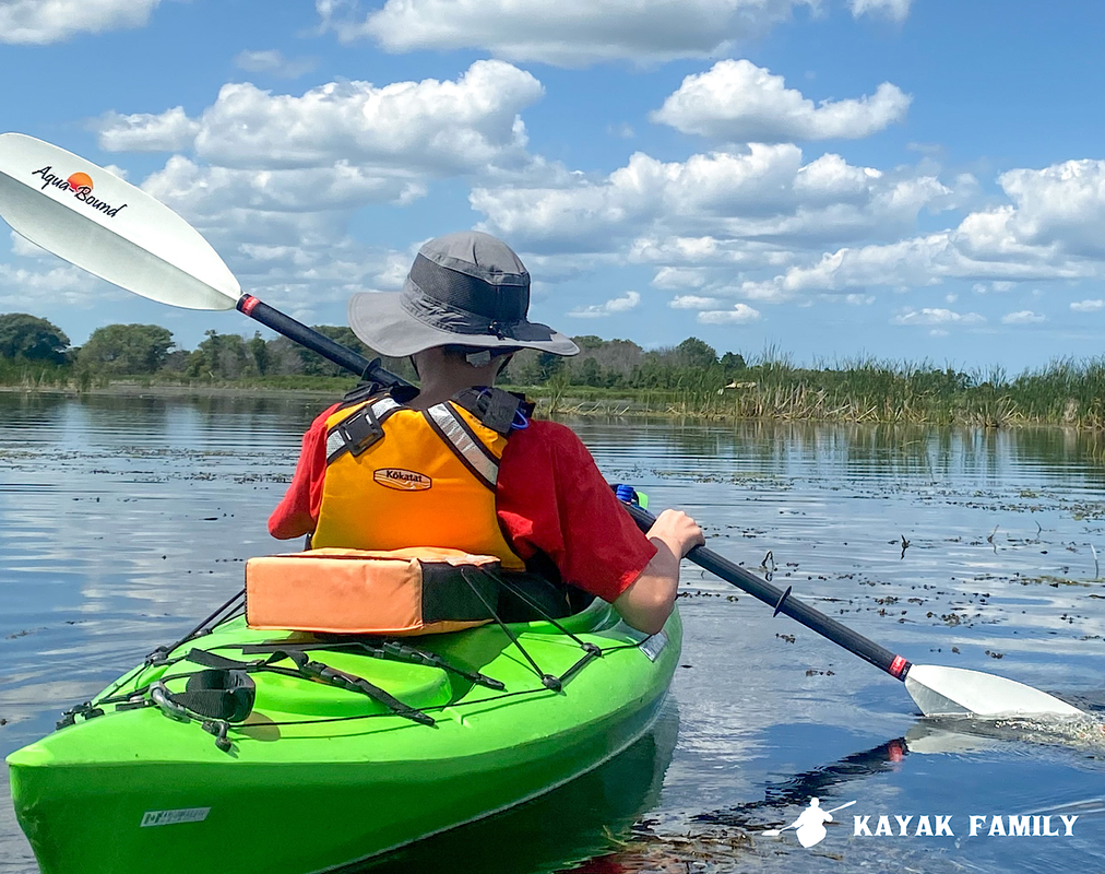 Boy with red shirt, Kokatat life jacket, AquaBound paddle and Green Clearwater Muskoka kayak on open marsh