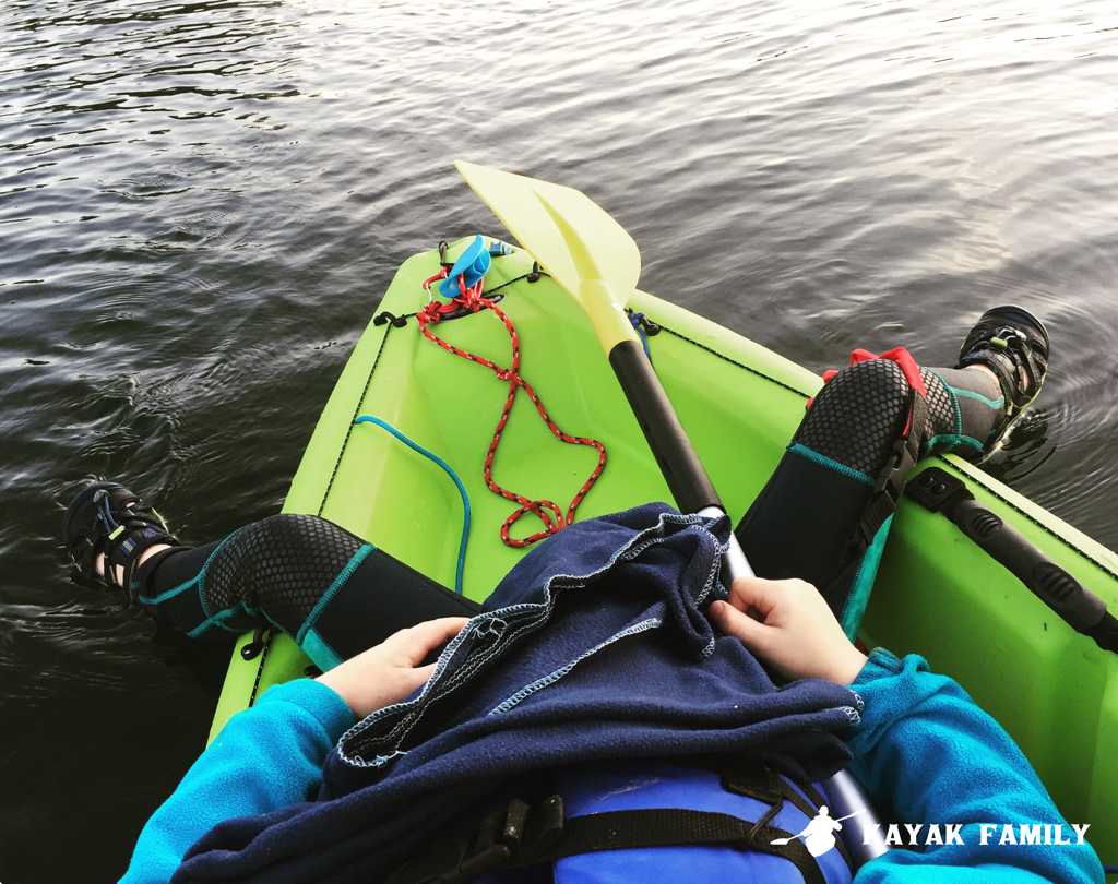 Child relaxes in back of kayak. Shown in wetsuit and life jacket. 